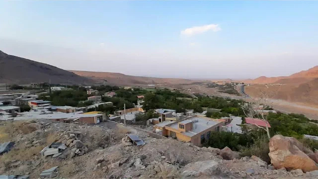 بام‌ها و باغ‌های سبز در پشت پیش‌زمینه سنگی با تپه‌ها در پس‌زمینه