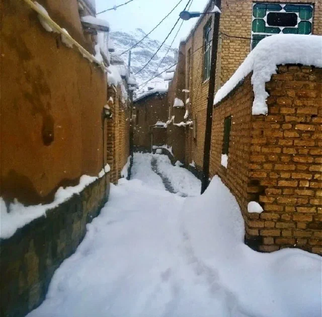 کوچه باریک پوشیده از برف میان دیوارهای آجری و خاکی‌رنگ