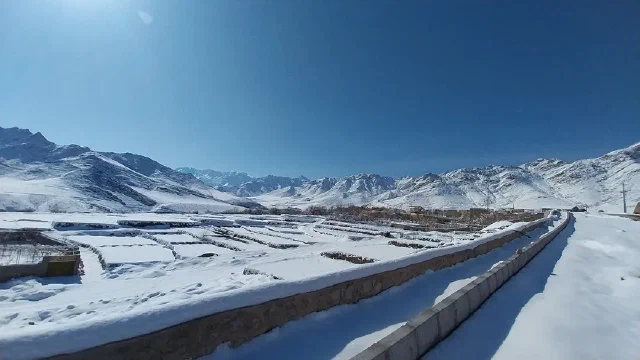زمین‌ها و کوه‌های پوشیده از برف کنار مسیر دیواردار زیر آسمان آبی و صاف
